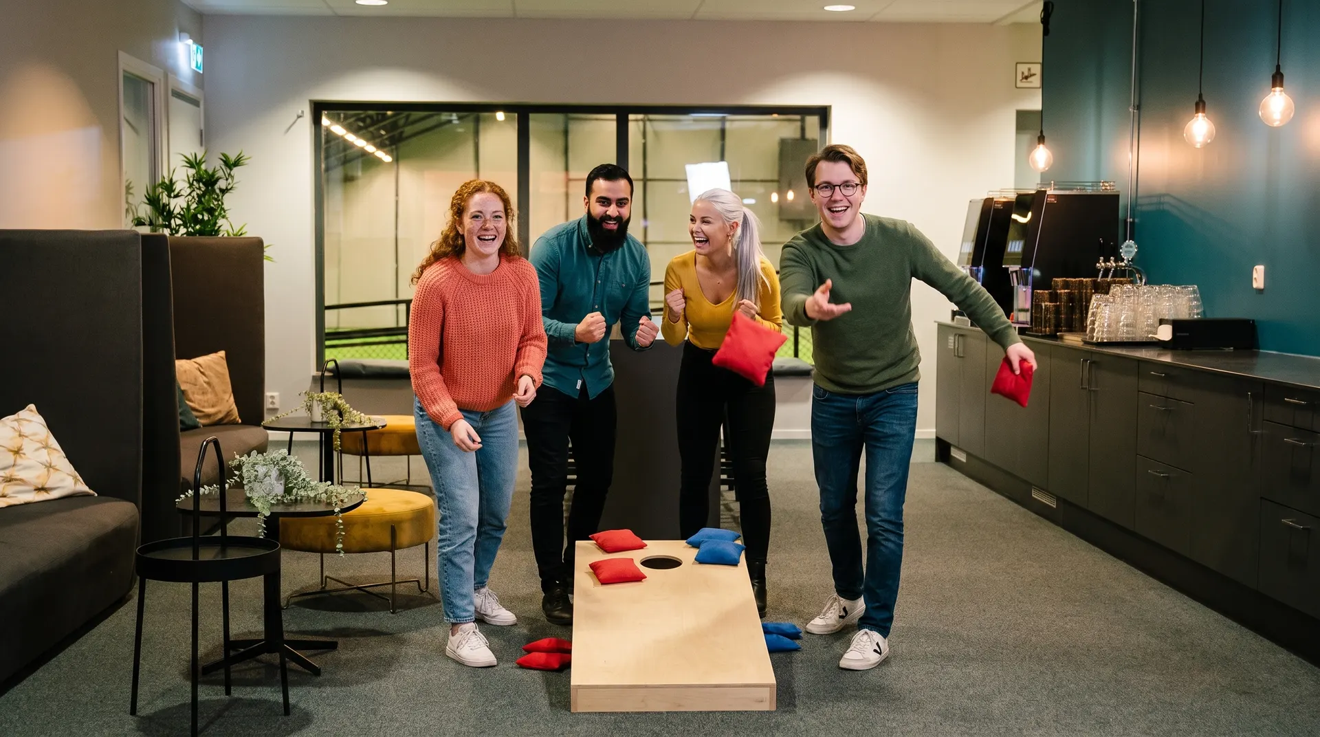Fyra vänner spelar cornhole i loungen på Kviberg Park med utsikt över inomhusplanen.